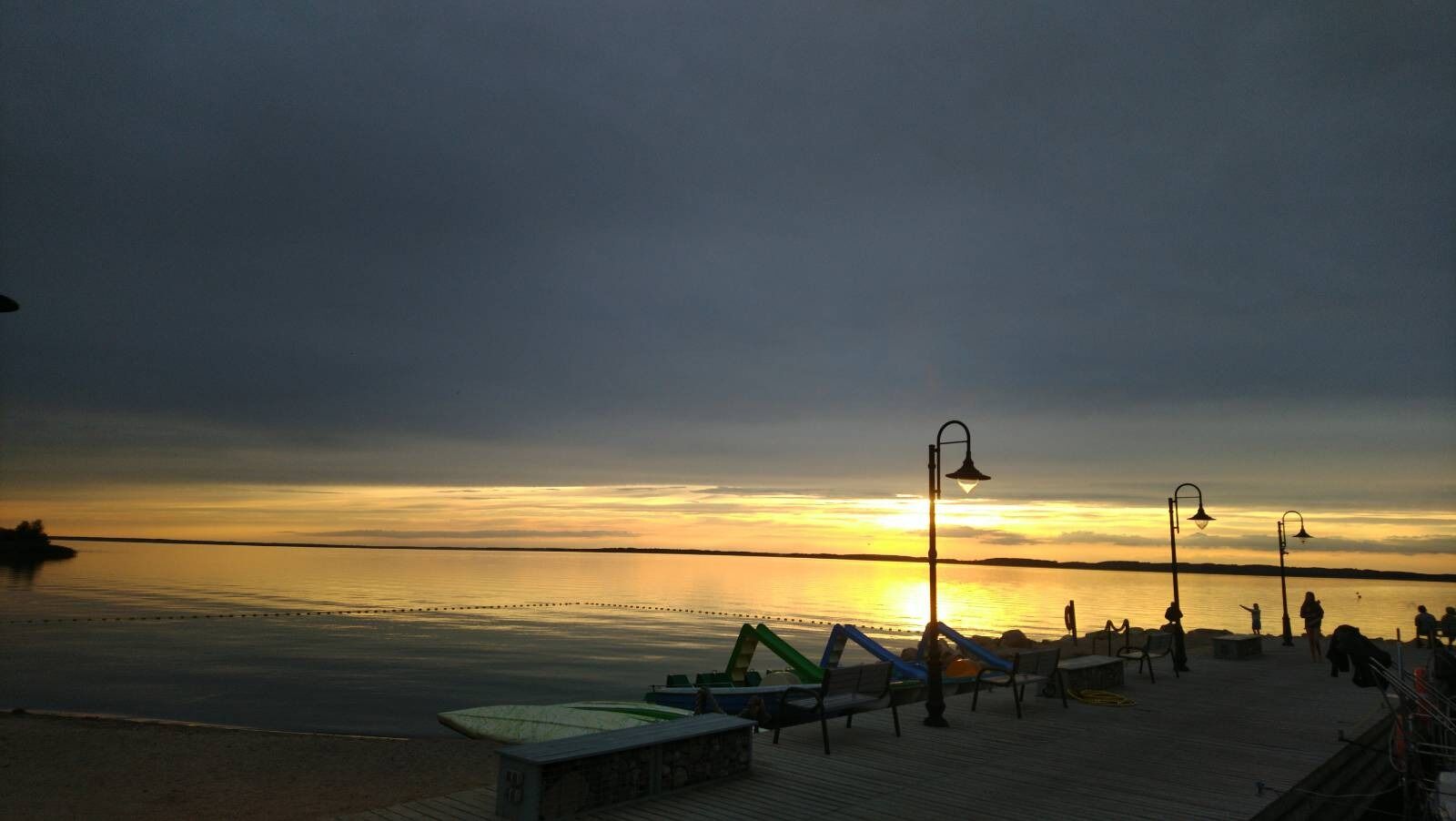 Beautiful sunset over a lake, gray sky, beach. A small pier with some lamp posts. Serene.